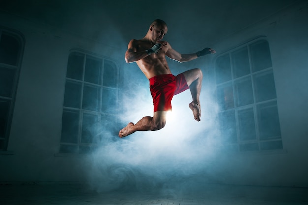 Photo gratuite le jeune athlète masculin kickboxing sur une fumée bleue