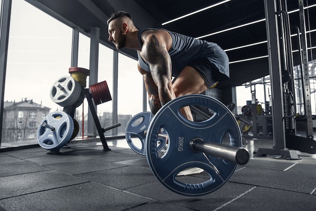 Jeune athlète musclé pratiquant des tractions dans une salle de sport avec haltères