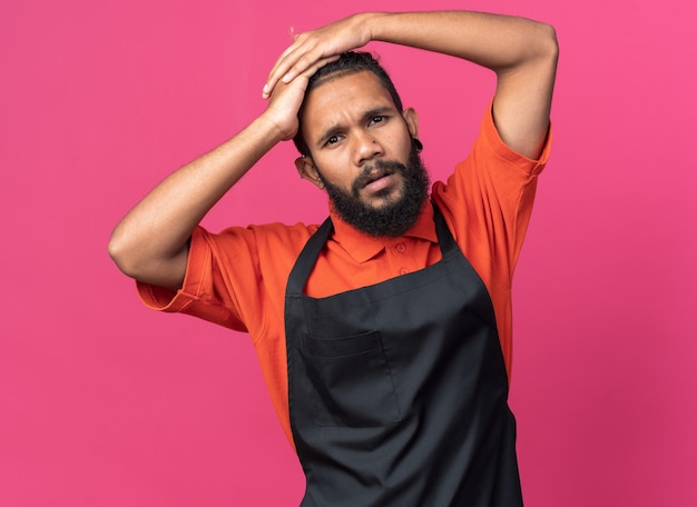 Jeune barbier afro-américain confus en uniforme gardant les mains sur la tête