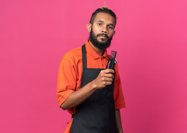 Jeune barbier afro-américain en uniforme tenant un peigne et une tondeuse à cheveux