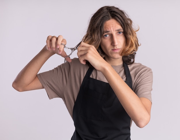 Jeune barbier effrayé en uniforme se coupant les cheveux avec des ciseaux