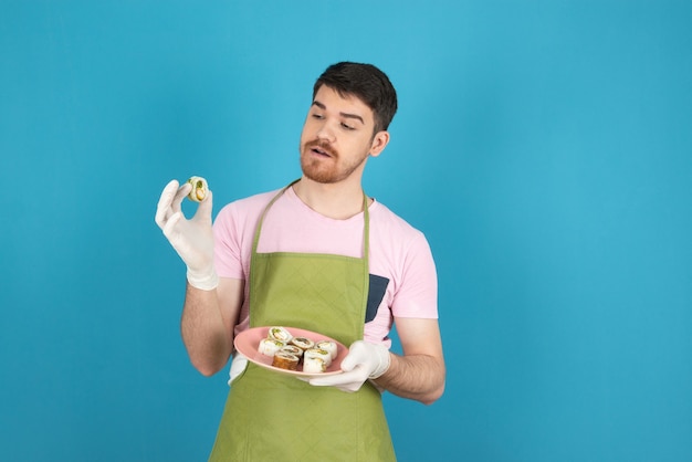 Jeune barbu regardant des petits pains faits maison sur un bleu.