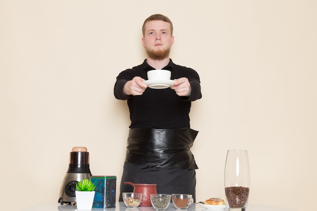 Jeune barista en costume de travail noir avec des ingrédients et du matériel de café graines de café brun sur blanc