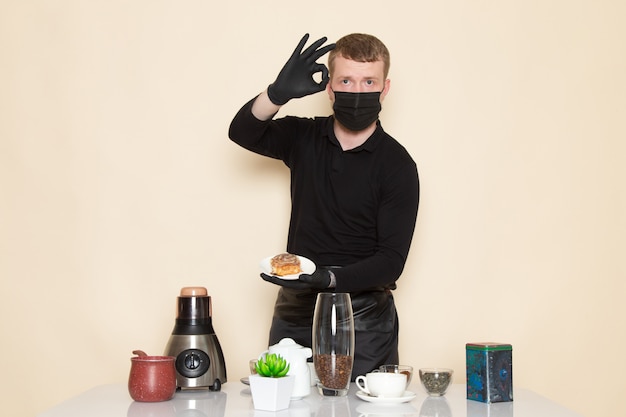 Photo gratuite jeune barista en costume de travail noir avec des ingrédients et du matériel de café graines de café brun portant un masque stérile noir sur blanc