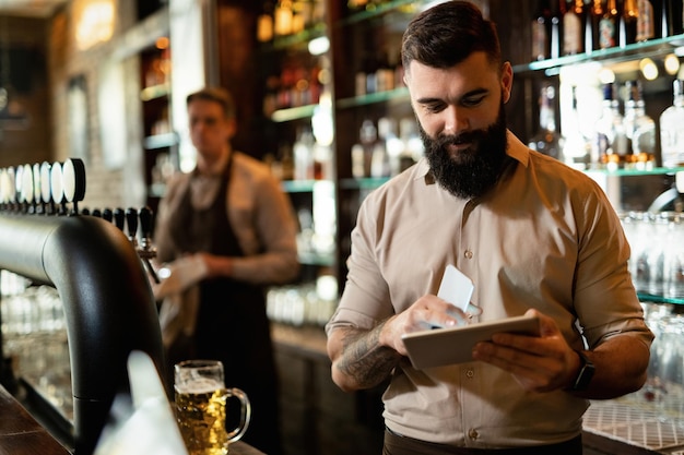 Jeune barista heureux travaillant dans un bar et surfant sur le net sur le pavé tactile.