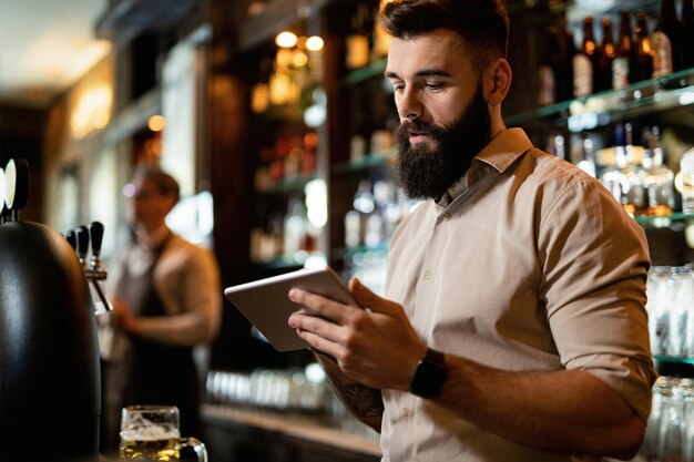 Jeune barman utilisant une tablette numérique tout en travaillant dans un pub