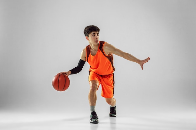 Jeune basketteur de l'équipe portant la formation de vêtements de sport, pratiquant en action, mouvement en course isolé sur mur blanc