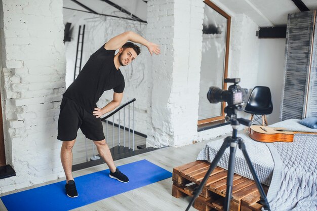 Le jeune et beau blogueur fitness enregistre une vidéo pour son blog et montre comment faire la bonne inclinaison sur le côté, dans une pièce de style loft