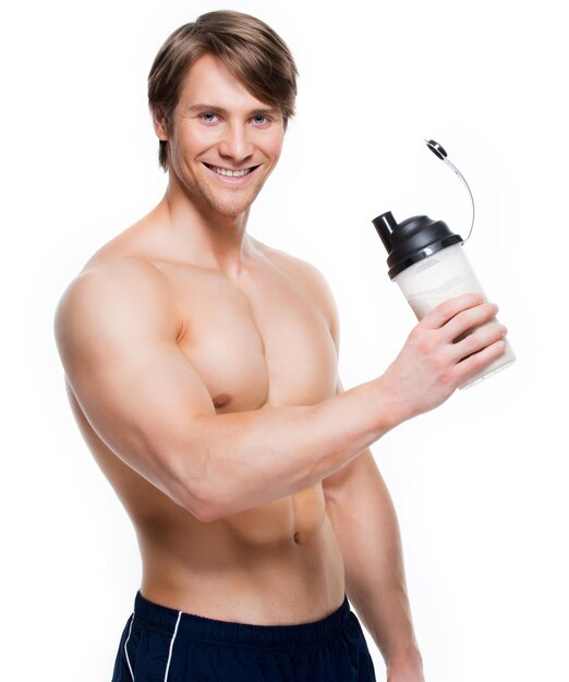 Jeune beau bodybuilder avec une bouteille posant sur un mur blanc.
