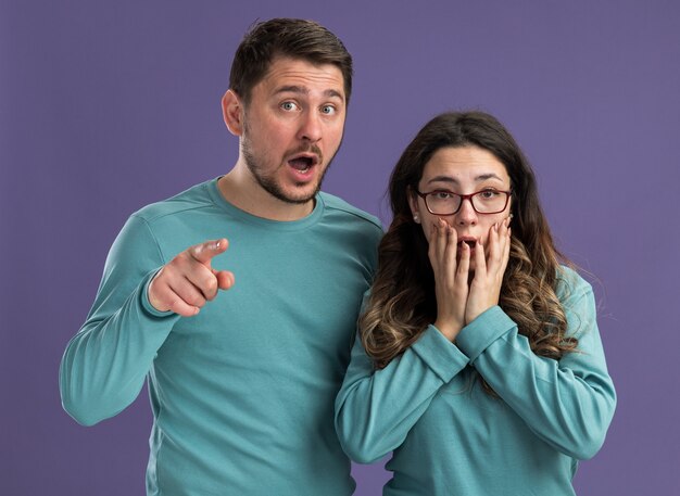 Jeune beau couple en bleu vêtements décontractés homme et femme étonnés et surpris debout sur un mur violet