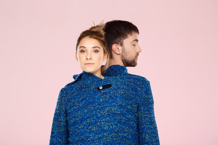 Photo gratuit jeune beau couple dans un pull en tricot bleu posant souriant s'amuser sur le mur rose clair