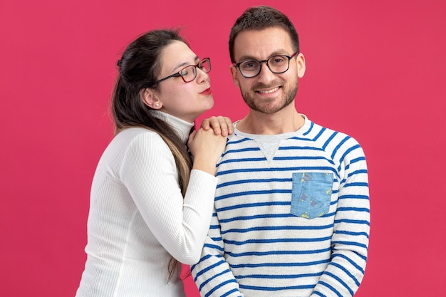 Jeune beau couple dans des vêtements décontractés femme heureuse va embrasser son petit ami souriant célébrant la Saint-Valentin debout sur le mur rose