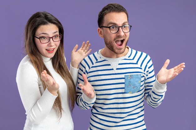 Jeune beau couple dans des vêtements décontractés heureux et surpris homme et femme à la recherche d'un concept de jour de valentines asidesmiling debout sur un mur violet