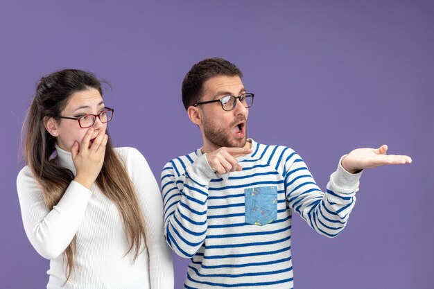 Jeune beau couple dans des vêtements décontractés surpris homme et femme regardant de côté Saint Valentin debout sur fond violet