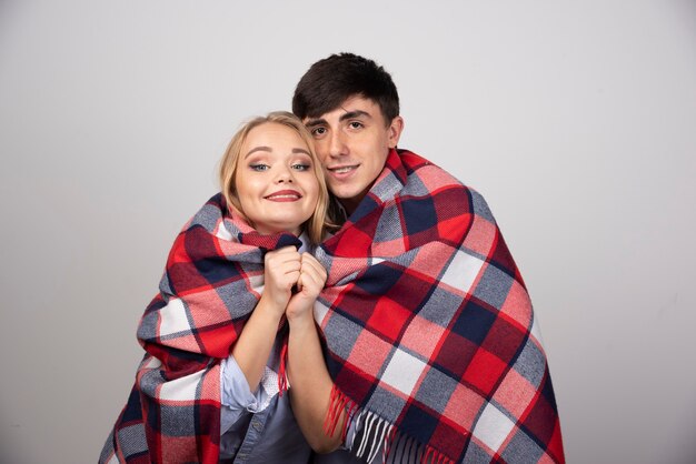 Jeune beau couple debout dans une couverture à carreaux et souriant