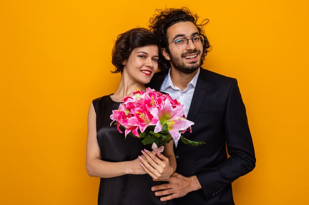 Jeune beau couple heureux homme et femme avec bouquet de fleurs souriant joyeusement embrassant heureux en amour