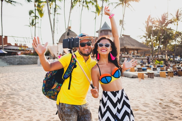 Jeune beau couple hipster amoureux sur la plage tropicale, prenant selfie photo sur smartphone, lunettes de soleil, tenue élégante, vacances d'été, s'amuser, souriant, heureux, coloré, émotion positive