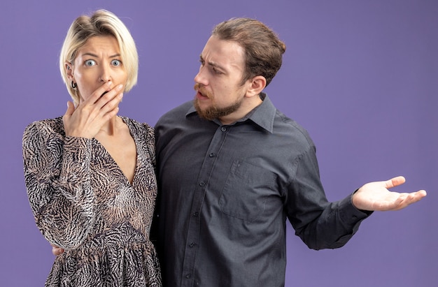 Jeune beau couple homme confus et mécontent de parler à sa petite amie étonné concept de jour de valentines debout sur le mur violet