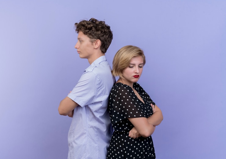 Photo gratuit jeune beau couple homme et femme debout dos à dos fronçant les sourcils debout sur le mur bleu