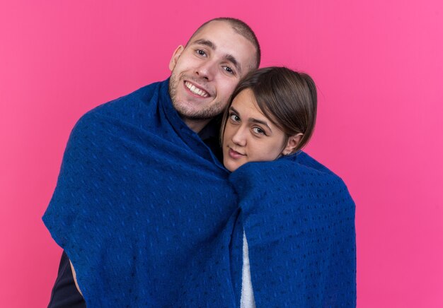 Jeune beau couple homme et femme enveloppé dans une couverture heureux en amour souriant joyeusement debout