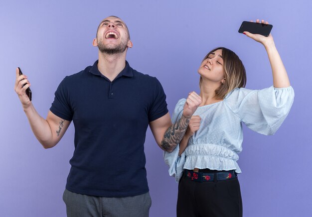 Jeune beau couple homme et femme tenant des smartphones heureux et excités se réjouissant de leur succès debout