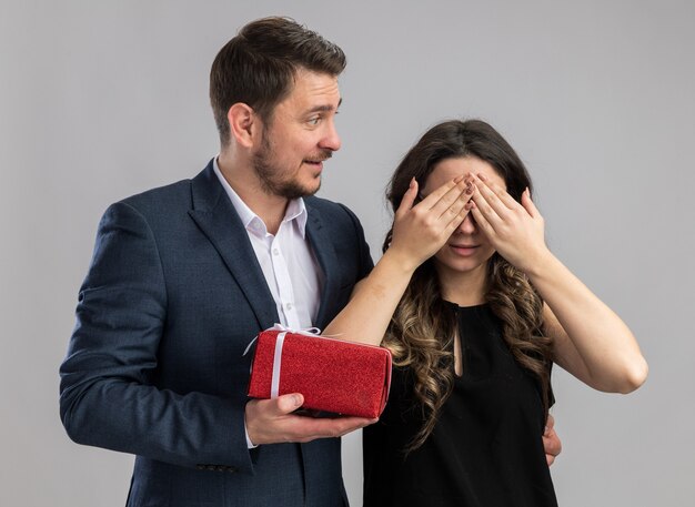 Jeune beau couple homme heureux donnant un cadeau à sa charmante petite amie pendant qu'elle se couvre les yeux heureux amoureux célébrant la Saint-Valentin