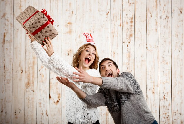 Jeune beau couple se battre pour un cadeau de Noël sur un mur en bois