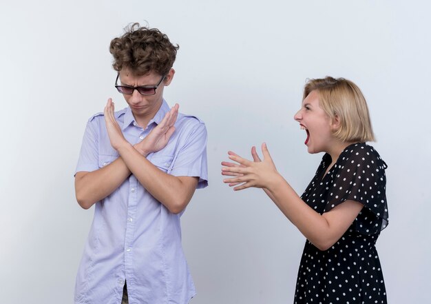 Jeune beau couple se quereller femme criant sur son petit ami qui montrant le geste d'arrêt avec hfrowning face au mur blanc