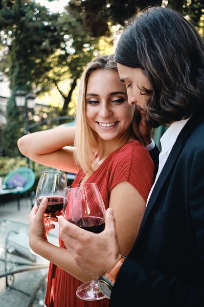 Jeune beau couple sensuel buvant joyeusement du vin rouge à la date du restaurant en plein air