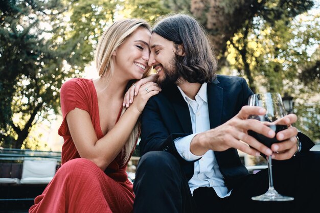 Jeune beau couple sensuel avec un verre de vin rouge parlant joyeusement à un rendez-vous au restaurant en plein air