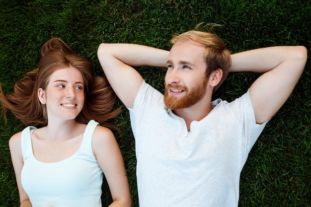 Jeune beau couple souriant, couché sur l'herbe dans le parc. Tiré d'en haut.