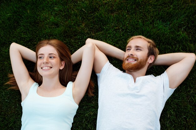 Jeune beau couple souriant, couché sur l'herbe dans le parc. Tiré d'en haut.