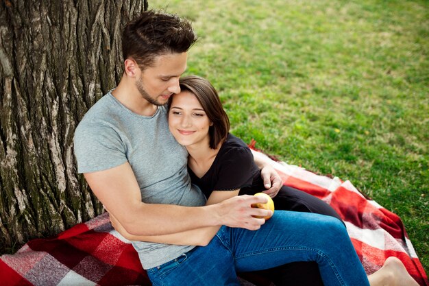 Jeune beau couple souriant, reposant sur un pique-nique dans le parc.