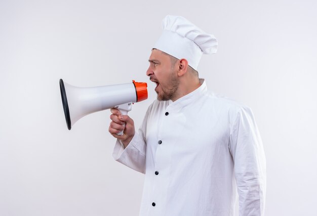 Jeune beau cuisinier en uniforme de chef parlant par le haut-parleur à côté isolé sur l'espace blanc