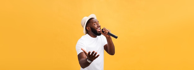 Photo gratuite jeune beau garçon afro-américain chantant émotionnel avec microphone isolé sur fond jaune