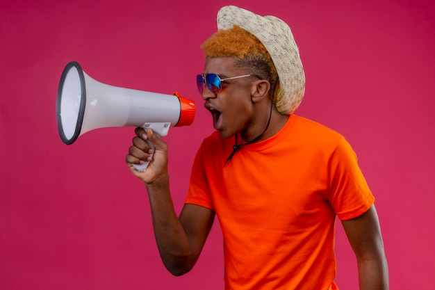 Jeune beau garçon au chapeau d'été portant un t-shirt orange criant au mégaphone