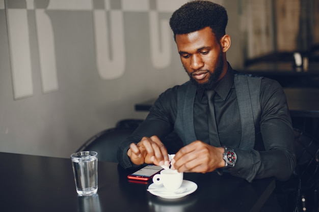 Un jeune et beau garçon à la peau sombre dans un costume noir assis dans un café