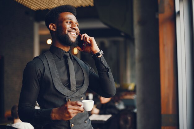 Un jeune et beau garçon à la peau sombre dans un costume noir debout dans un café