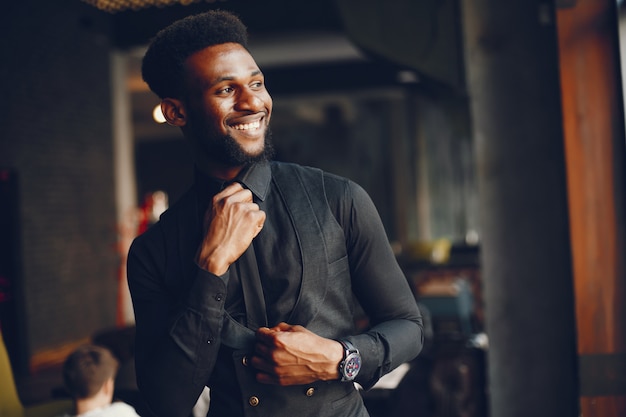 Un jeune et beau garçon à la peau sombre dans un costume noir debout dans un café