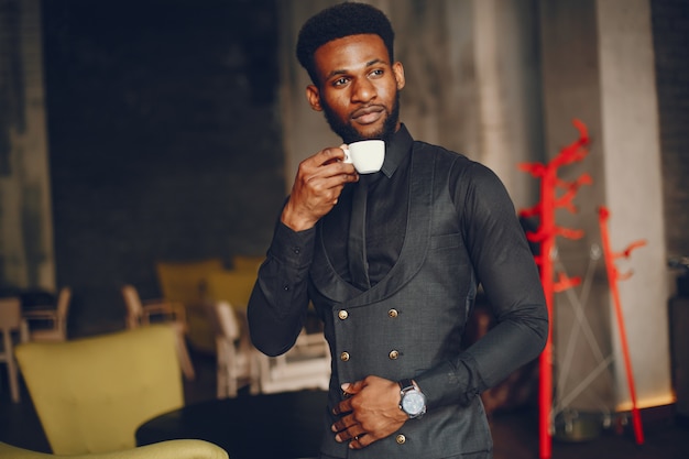 Un jeune et beau garçon à la peau sombre dans un costume noir debout dans un café