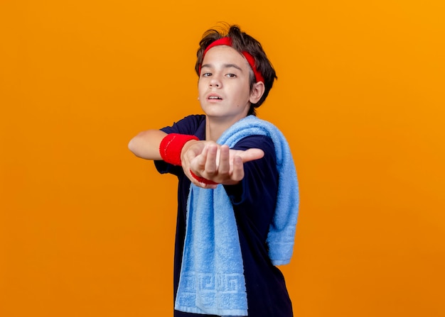 Photo gratuite jeune beau garçon sportif portant bandeau et bracelets avec appareil dentaire et serviette sur l'épaule debout en vue de profil isolé sur mur orange