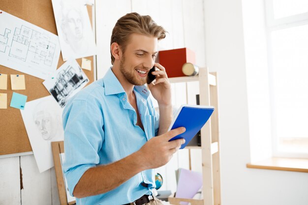 Jeune, beau, homme affaires, debout, table, conversation, téléphone, tenue, cahier