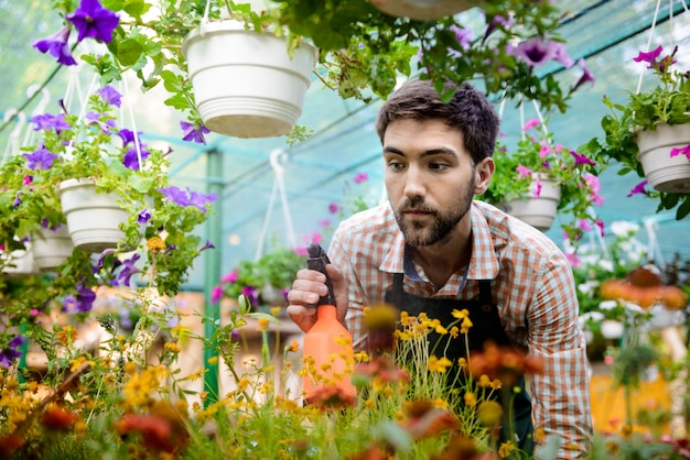 Jeune beau jardinier gai souriant, arrosant, en prenant soin des fleurs