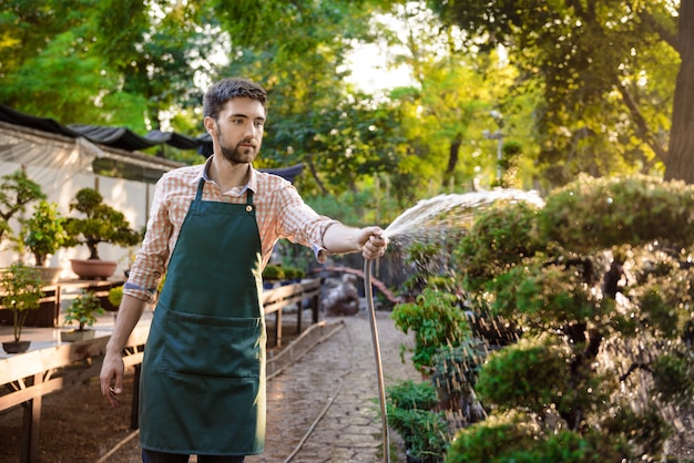 Jeune beau jardinier gai souriant, arrosant, en prenant soin des plantes