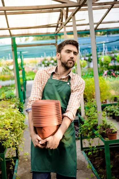 Jeune beau jardinier gai tenant des pots parmi les plantes