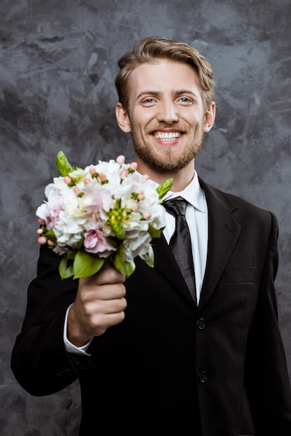 Jeune beau marié souriant, tenant un bouquet de mariée