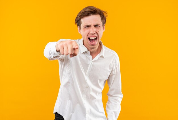 Jeune beau mec en colère portant une chemise blanche vous montrant un geste isolé sur un mur orange