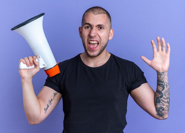 Jeune beau mec en colère portant un t-shirt noir tenant un haut-parleur isolé sur fond bleu