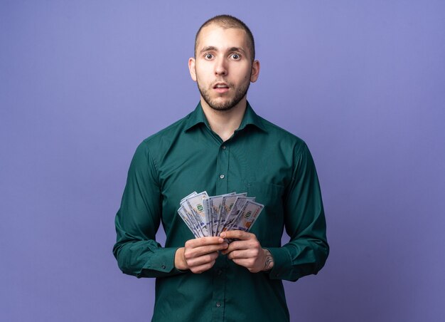 Jeune beau mec confus portant une chemise verte tenant de l'argent