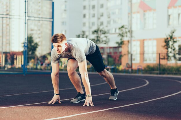 Jeune beau mec le matin sur le stade. Il porte des vêtements de sport, écoute de la musique avec des écouteurs, va courir.